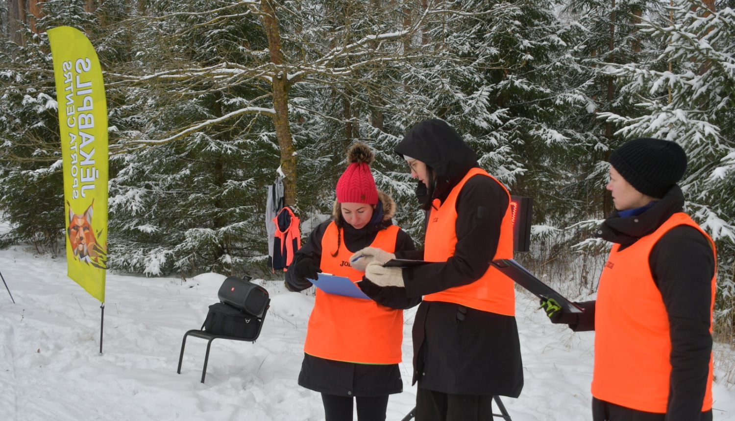 Pusstundas skrējiena ilustratīvs foto - cilvēki vestēs ziemīgā mešā skatās orientēšanās kartē