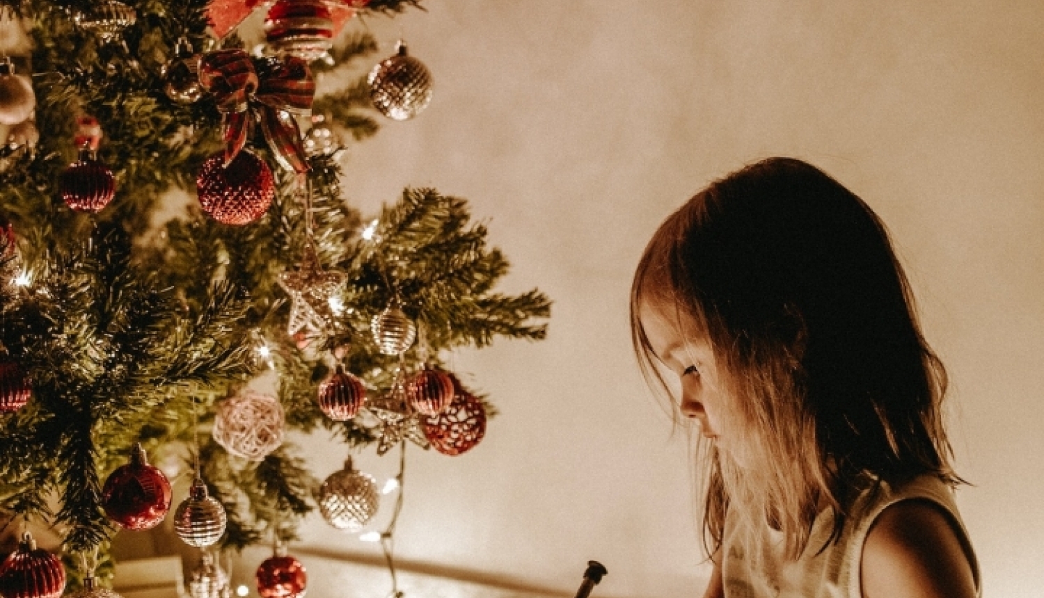 Bērns istabā norūpējies sēž un skatās uz Ziemassvētku eglīti