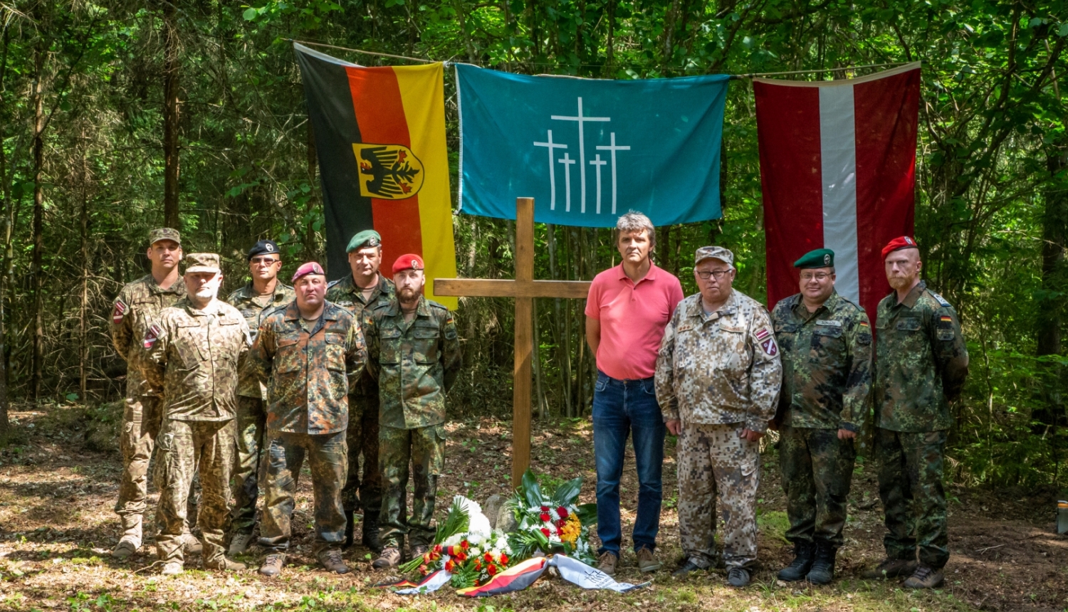 Bundesvēra karavīri, Zemessardzes un pašvaldības pārstāvis U.Skreivers stāv pie piemiņas krusta mežā, aizmugurē Vācijas un Latvijas karogi