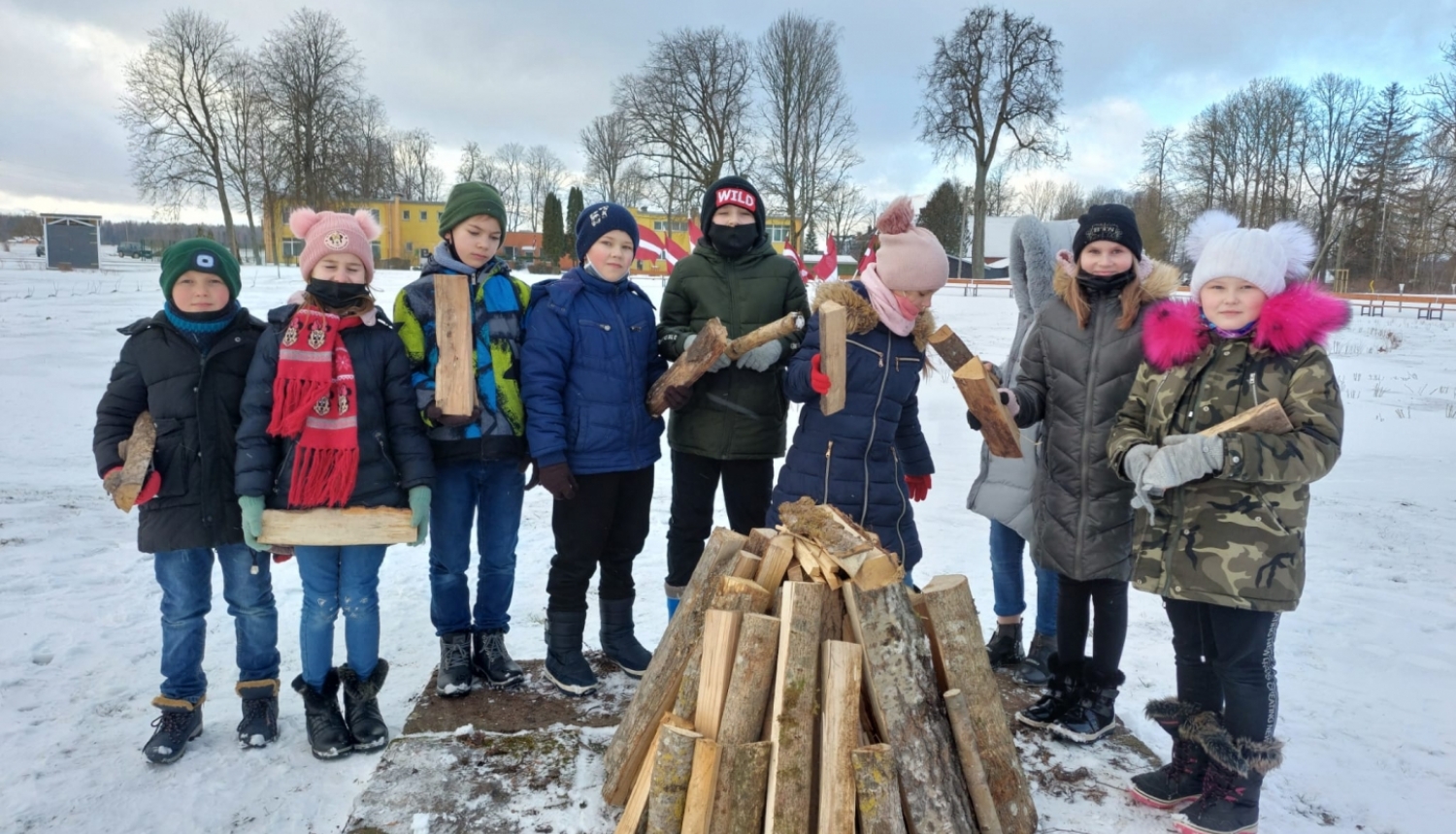 Skolēni stāv pusaplī aiz barikāžu ugunskura, turot rokās pagales
